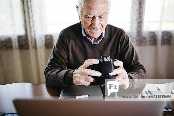 Senior photographer with laptop and digital camera at home