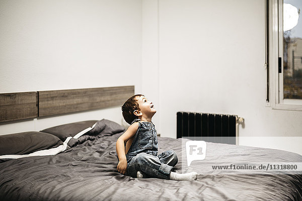Kleiner Junge,  der auf dem Bett seiner Eltern sitzt und etwas beobachtet.