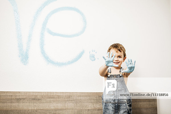Porträt eines lächelnden kleinen Jungen  der seine Handflächen voller hellblauer Farbe zeigt.