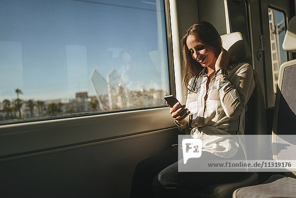 Lächelnde Frau im Zug beim Blick aufs Handy