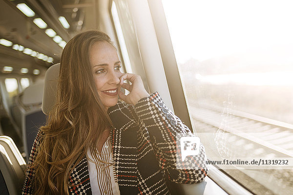 Lächelnde Frau im Zug mit Blick aus dem Fenster
