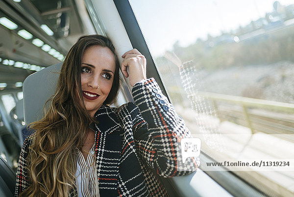 Lächelnde Frau im Zug mit Blick aus dem Fenster