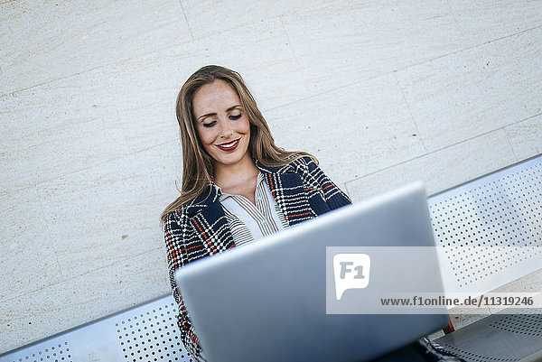 Geschäftsfrau auf einer Bank sitzend mit einem Laptop