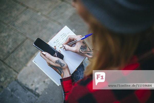 Tattooed woman's hand writing in notebook