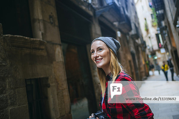 Spanien  Barcelona  Porträt einer lächelnden jungen Frau mit Kamera im Gothic Quarter
