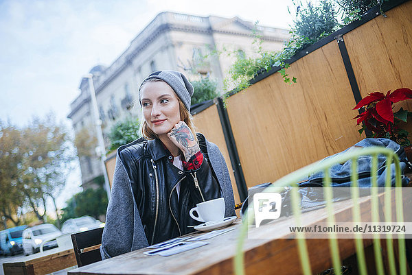Junge tätowierte Frau sitzt im Straßencafé