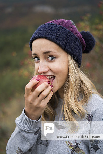 Porträt einer lächelnden jungen Frau  die einen Apfel im Freien isst.