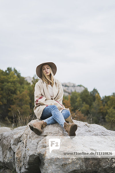 Junge Frau mit Hut auf Felsbrocken sitzend
