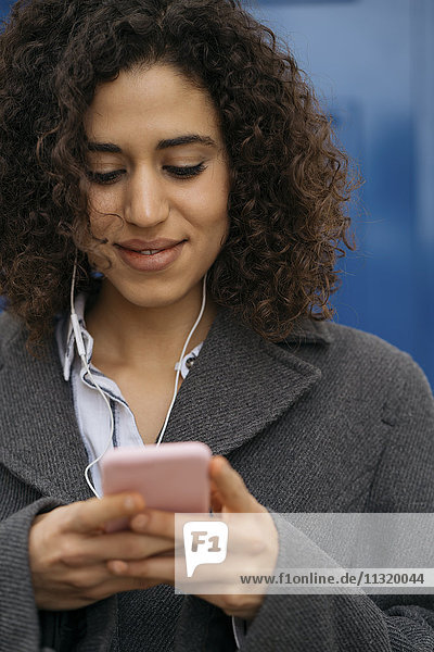Smiling young woman with earphones looking at mobile phone