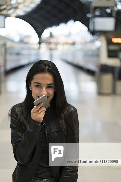 Glückliche junge Frau mit Handy am Bahnhof