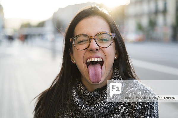 Porträt einer glücklichen jungen Frau mit einer Brille  die ihre Zunge herausstreckt.