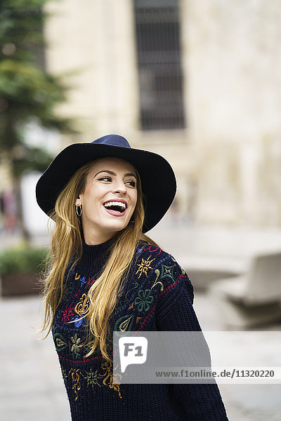 Porträt einer lachenden jungen Frau mit blauem Hut