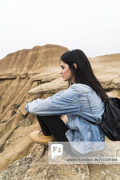 Spanien  Navarra  Bardenas Reales  junge Frau auf einem Felsen im Naturpark sitzend  mit Blick auf die Aussicht