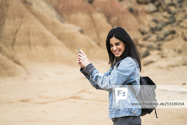 Spanien  Navarra  Bardenas Reales  lachende junge Frau im Naturpark mit Selfie mit Handy