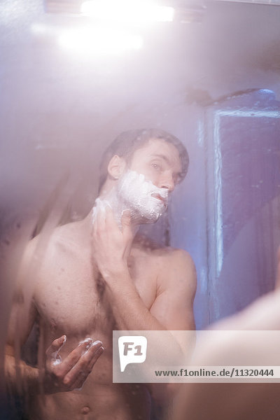 Mirror image of young man applying shaving foam