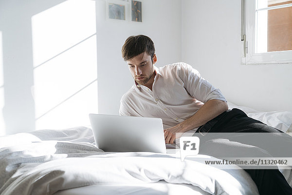 Junger Mann auf dem Bett liegend mit Laptop
