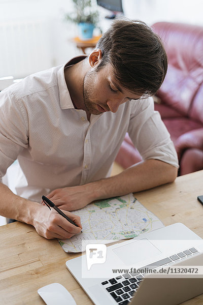 Young man with city map and laptop at home