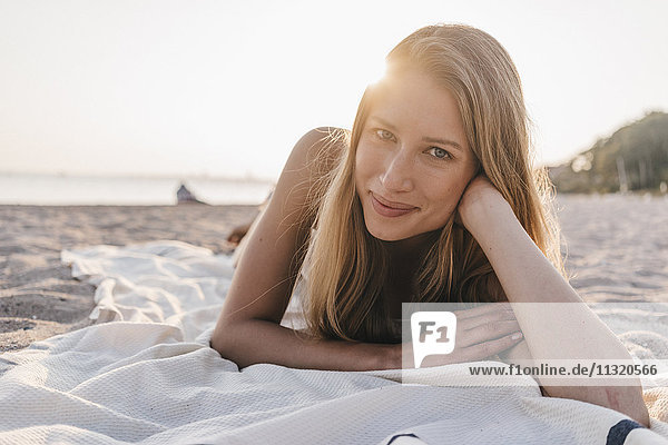 Porträt einer jungen Frau  die auf einer Decke am Strand liegt.