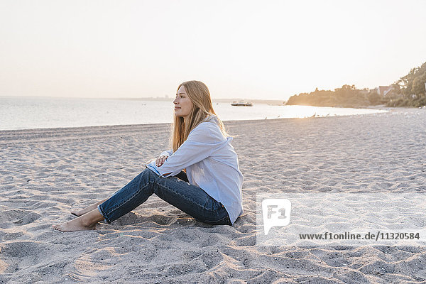Young woman sitting on the beach in the evening