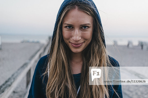 Porträt einer lächelnden jungen Frau mit Kapuzenjacke am Steg