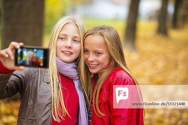 Zwei lächelnde Mädchen nehmen Selfie mit Handy im Herbst