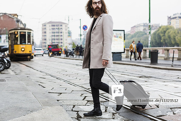 Stilvoller junger Mann mit kofferüberquerender Straßenbahn