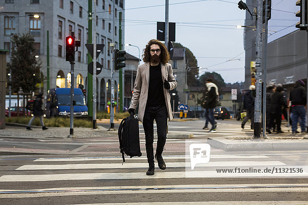 Stylish young man with bag crossing street on zebra crossing