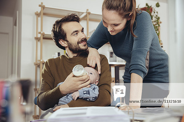 Mother looking at father feeding baby in home office