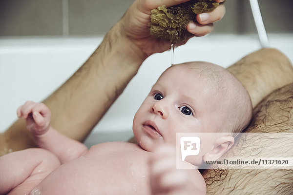 Father and baby taking a bath with a natural sponge