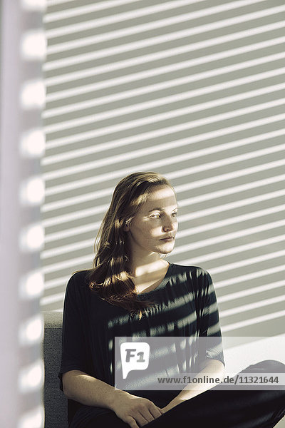 Portrait of serious young woman sitting in a shadowed room