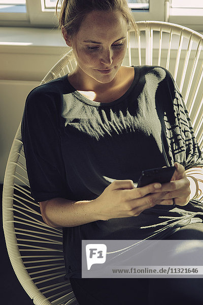 Young woman sitting in a chair looking at her cell phone