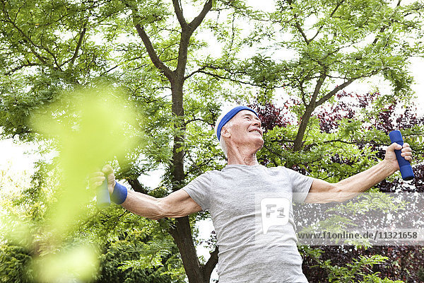 Senior Mann beim Fitnesstraining mit Kurzhanteln im Garten