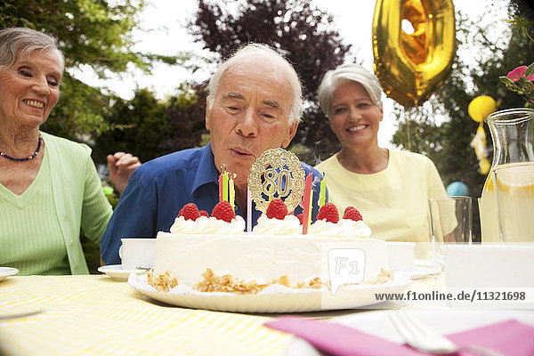 Senior Mann bläst Kerze auf 80. Geburtstagstorte