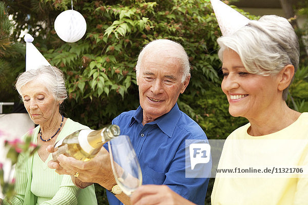 Leute  die im Garten feiern  Senioren  die Champagner ins Glas gießen.
