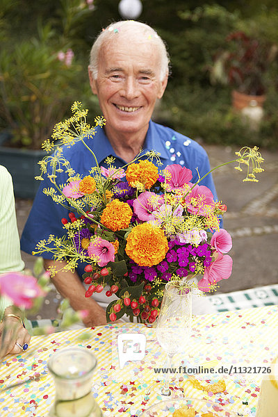 Älterer Mann am Tisch sitzend mit Blumenstrauß