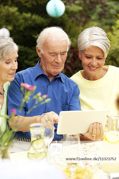 Älterer Mann beim Betrachten des digitalen Tabletts mit Gästen