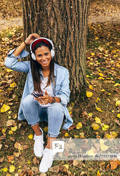 Young woman listening to music with her smartphone in a park in autumn