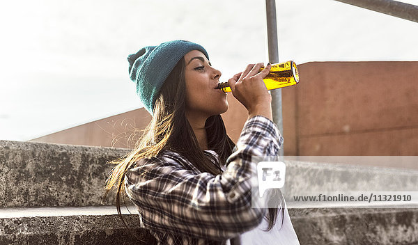 Young woman sitting on stairs drinking a beer from the bottle