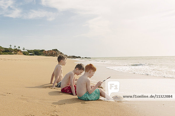 Drei Jungen sitzen am Strand.