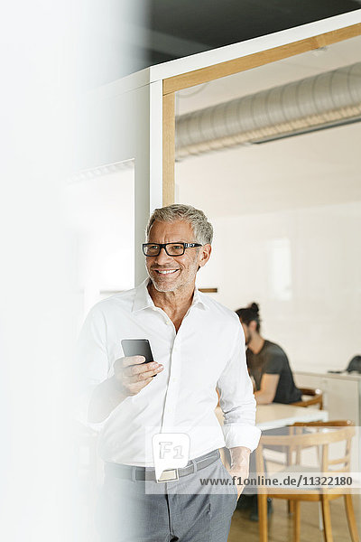 Smiling businessman with cell phone in office