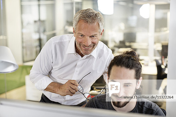 Two smiling men in office looking at computer monitor