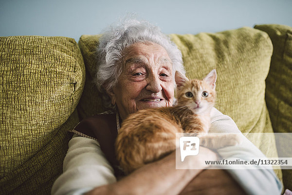 Porträt einer glücklichen Seniorin  die mit ihrer Katze auf der Couch kuschelt.