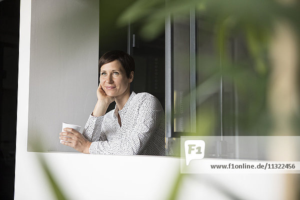 Lächelnde Frau mit Tasse Kaffee am Fenster