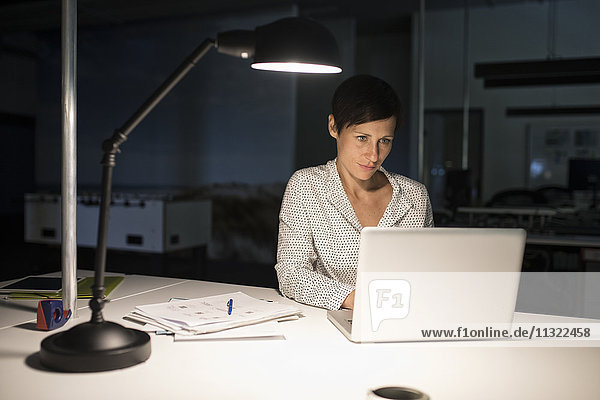 Geschäftsfrau im Büro mit Laptop im Dunkeln