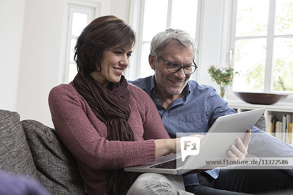 Smiling mature couple at home on the sofa using laptop