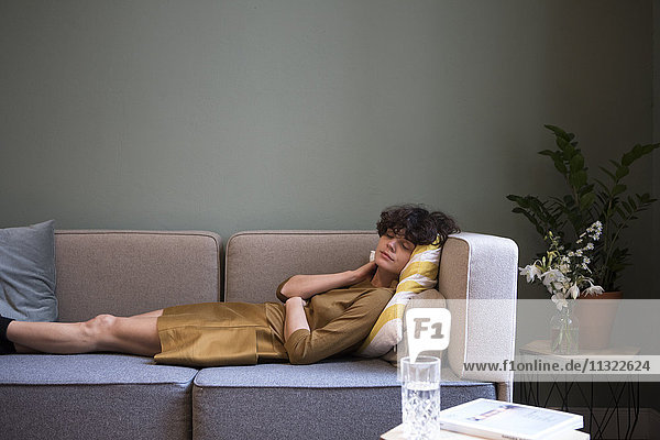 Junge Frau mit geschlossenen Augen entspannt auf der Couch zu Hause