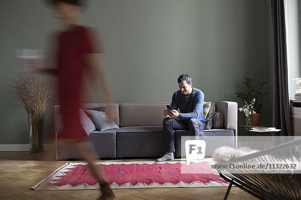 Man sitting on the couch in the living room while his girlfriend passing in the foreground