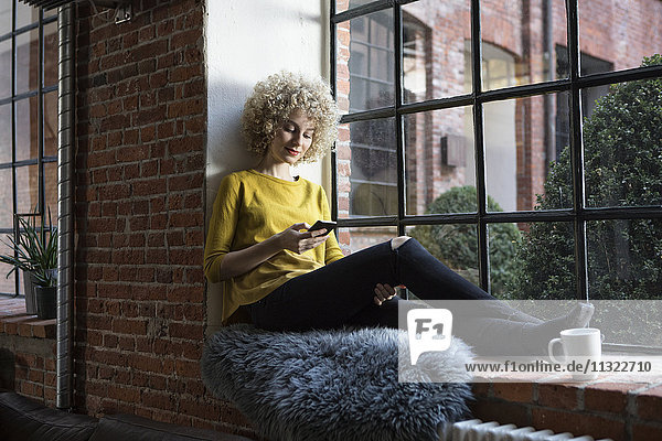 Junge Frau auf der Fensterbank sitzend  mit Smartphone