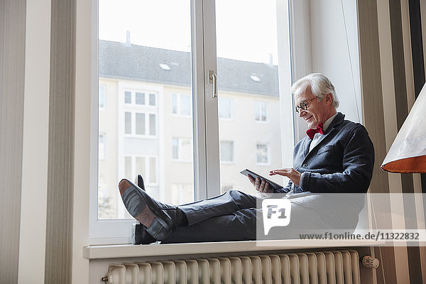 Älterer Mann auf der Fensterbank sitzend mit Tablette