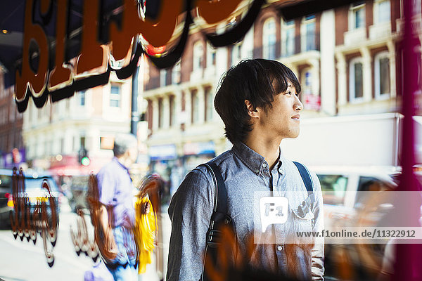 Young Japanese man enjoying a day out in London  walking past a shop window.